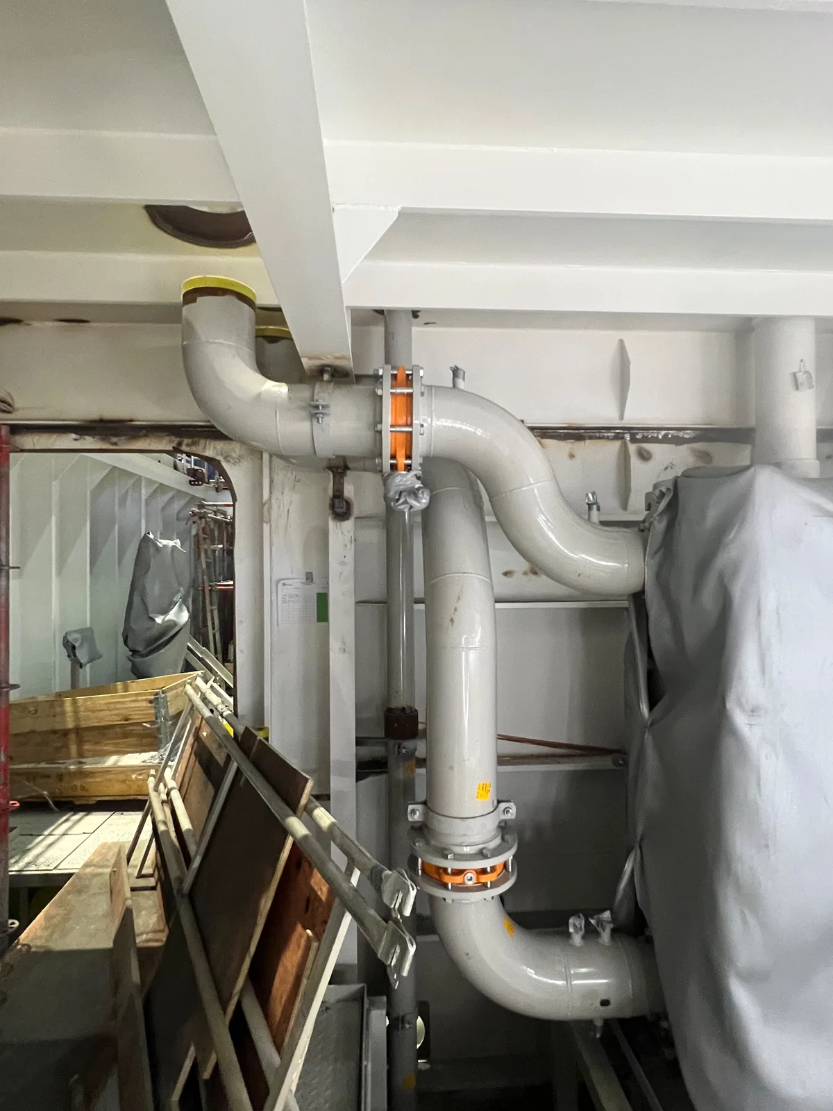 Large-bore pipe runs under a deckhead, with mechanical couplings on the vertical drop and anchors either side of them