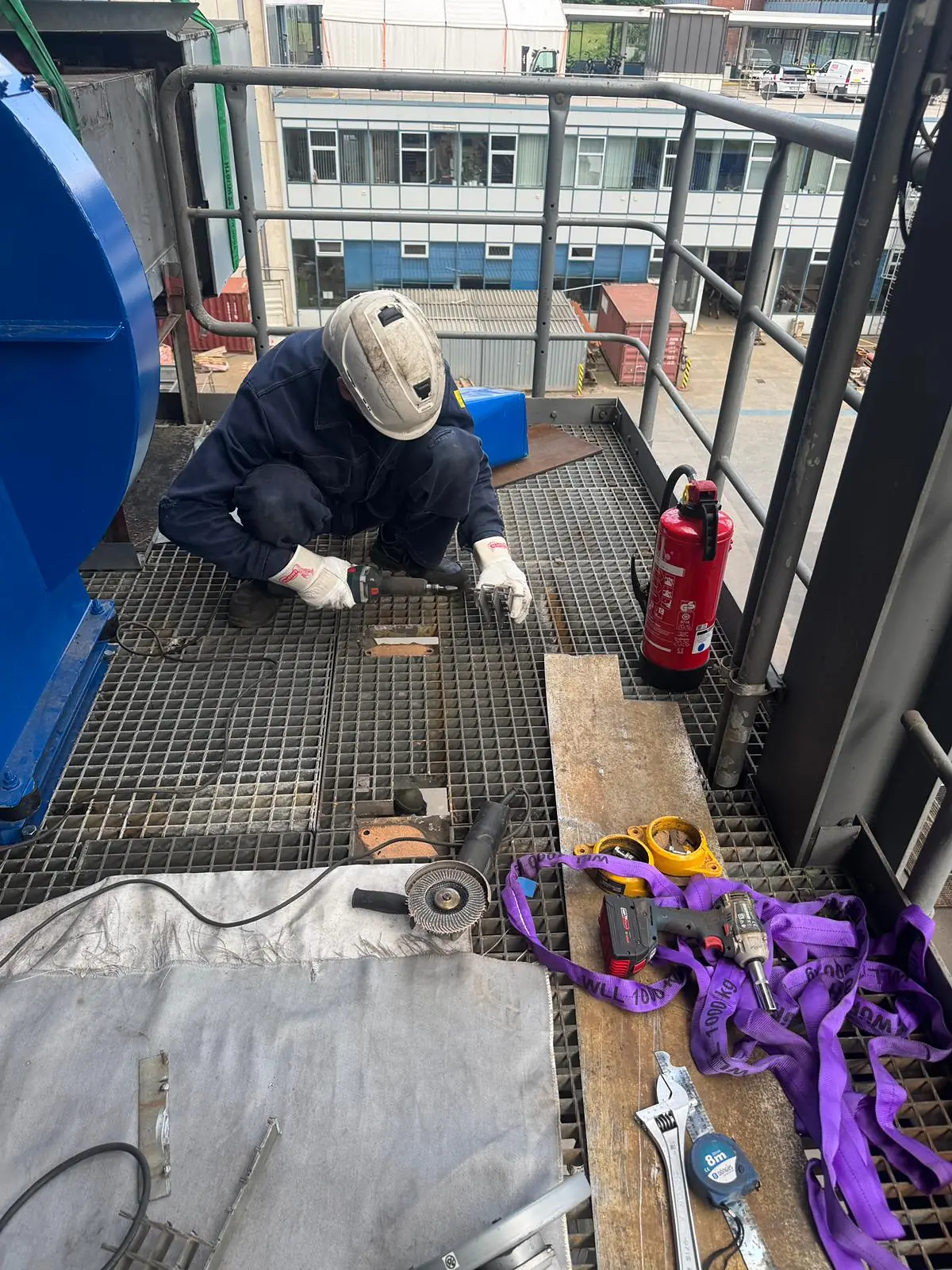 Worker at the base of the newly landed fan on the grating platform, with lifting slings, tools and a fire extinguisher laid out beside him