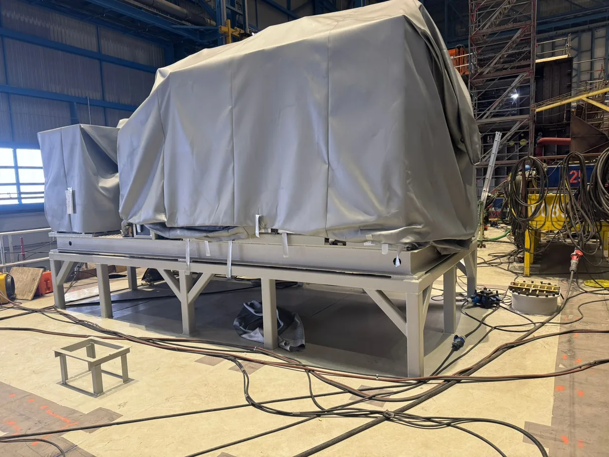 Machinery unit under protective covers on a fabricated steel frame in a shipyard hall
