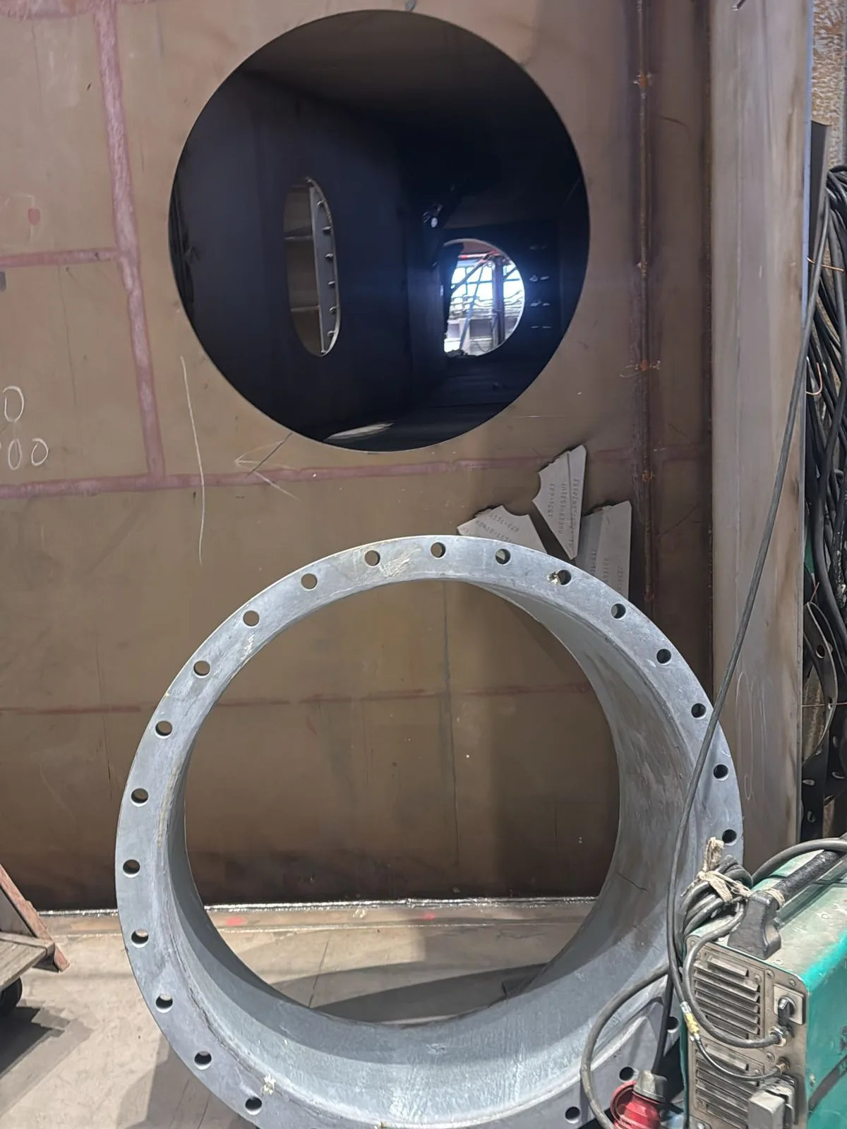 Circular opening cut in a bulkhead, with the penetration piece standing ready on the deck beside it