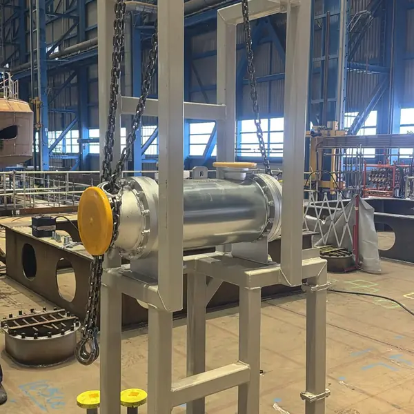Cylindrical steel unit in a fabricated frame, suspended on chain hoists over its marked position on the deck of a vessel under construction