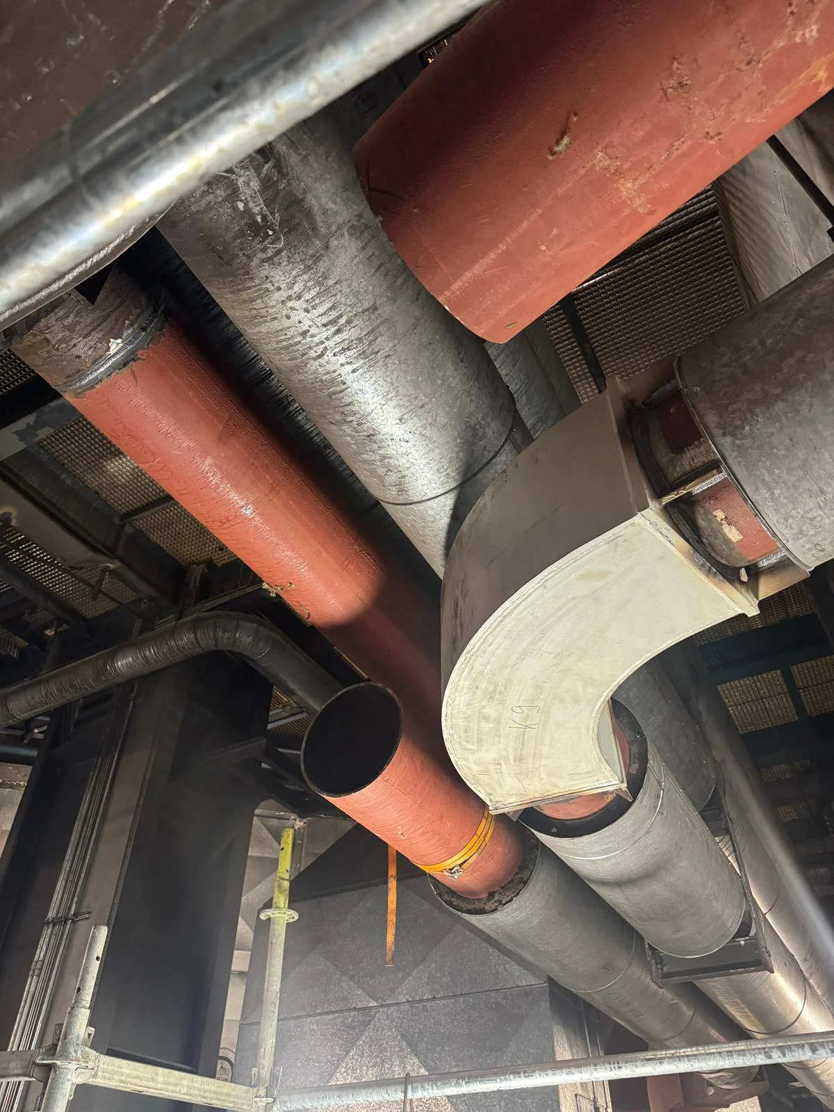 New large-bore pipework and a fabricated bend installed among existing lines and ducts inside an industrial plant