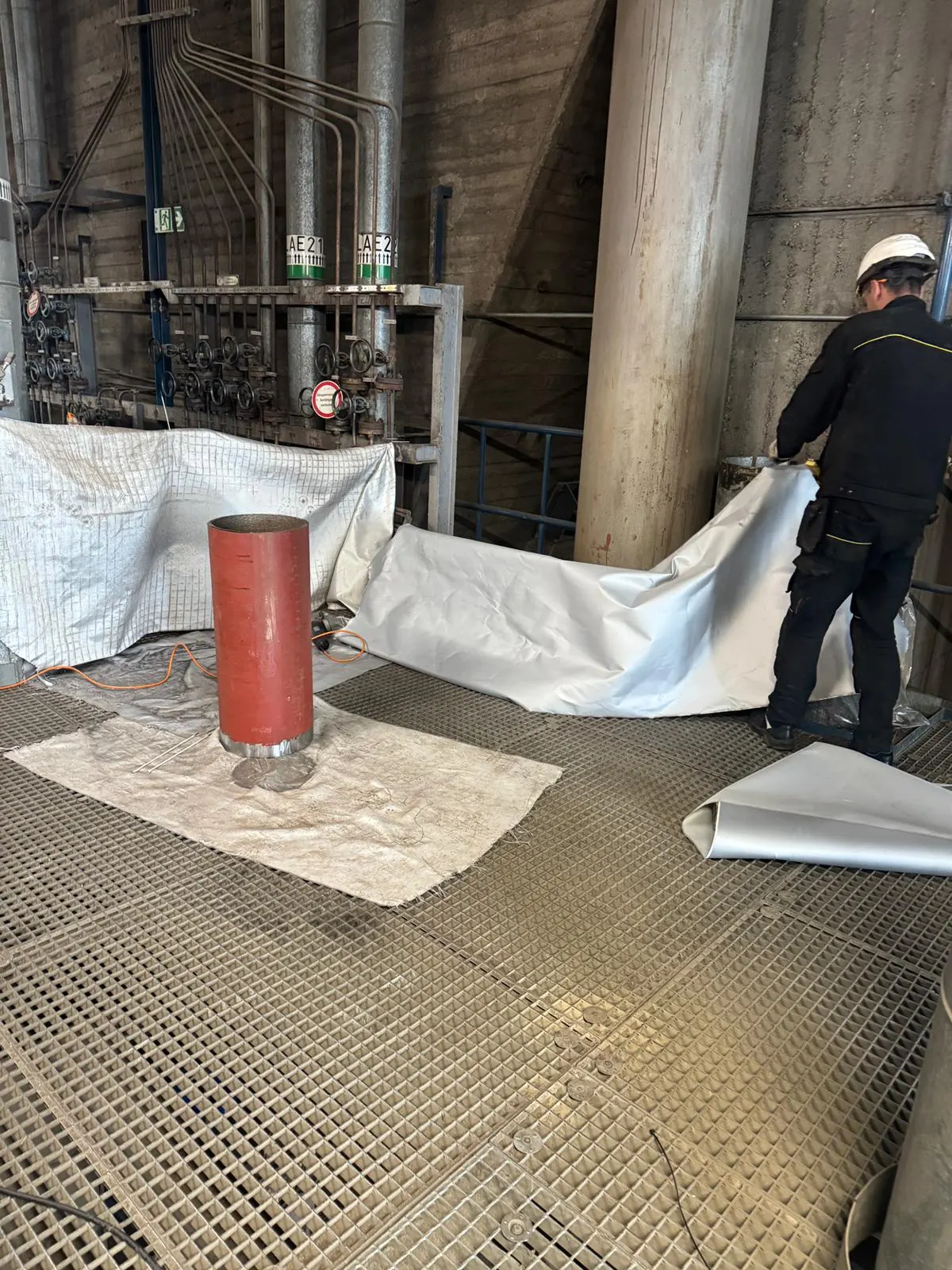 Protective sheeting and welding blankets laid over plant grating around a pipe spool standing ready for installation