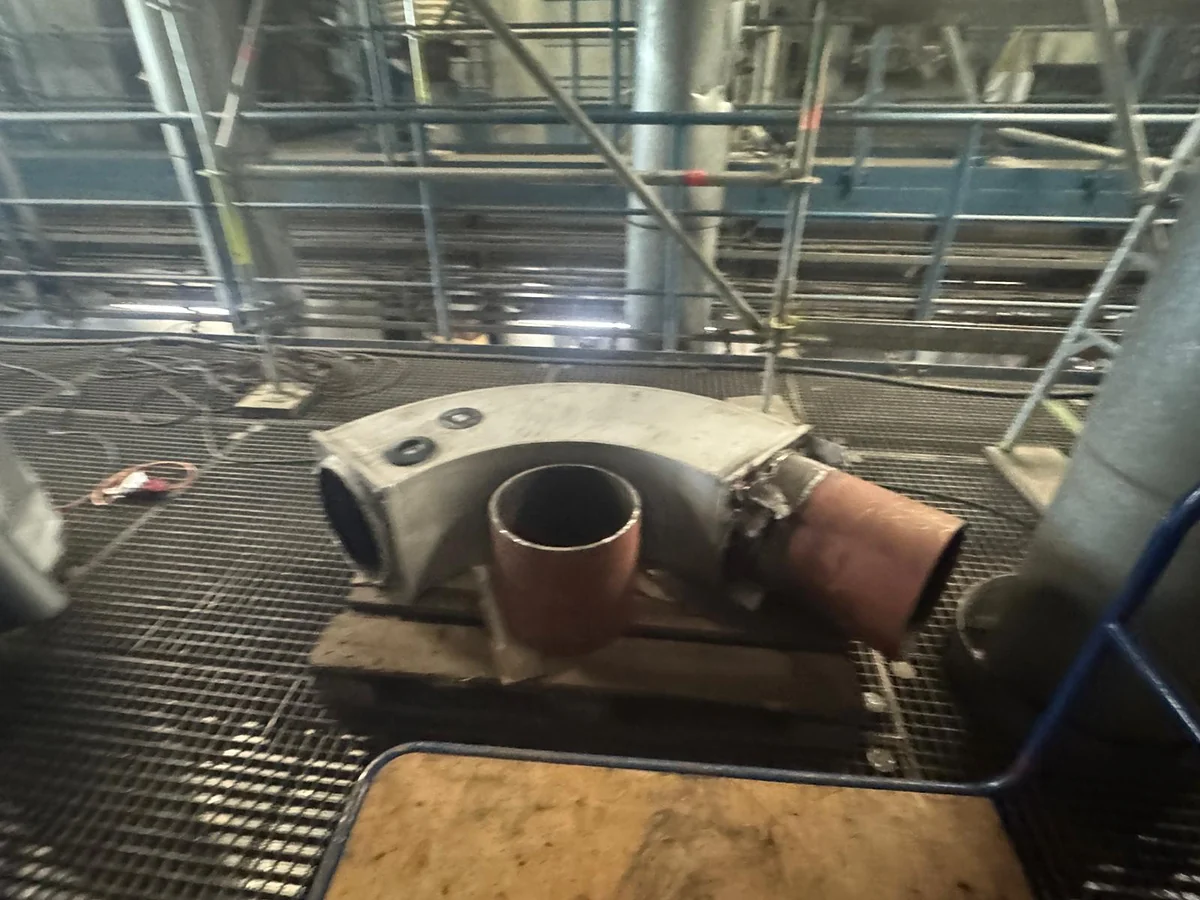 Prefabricated pipe bend with a welded branch and stub, standing on timber on plant grating