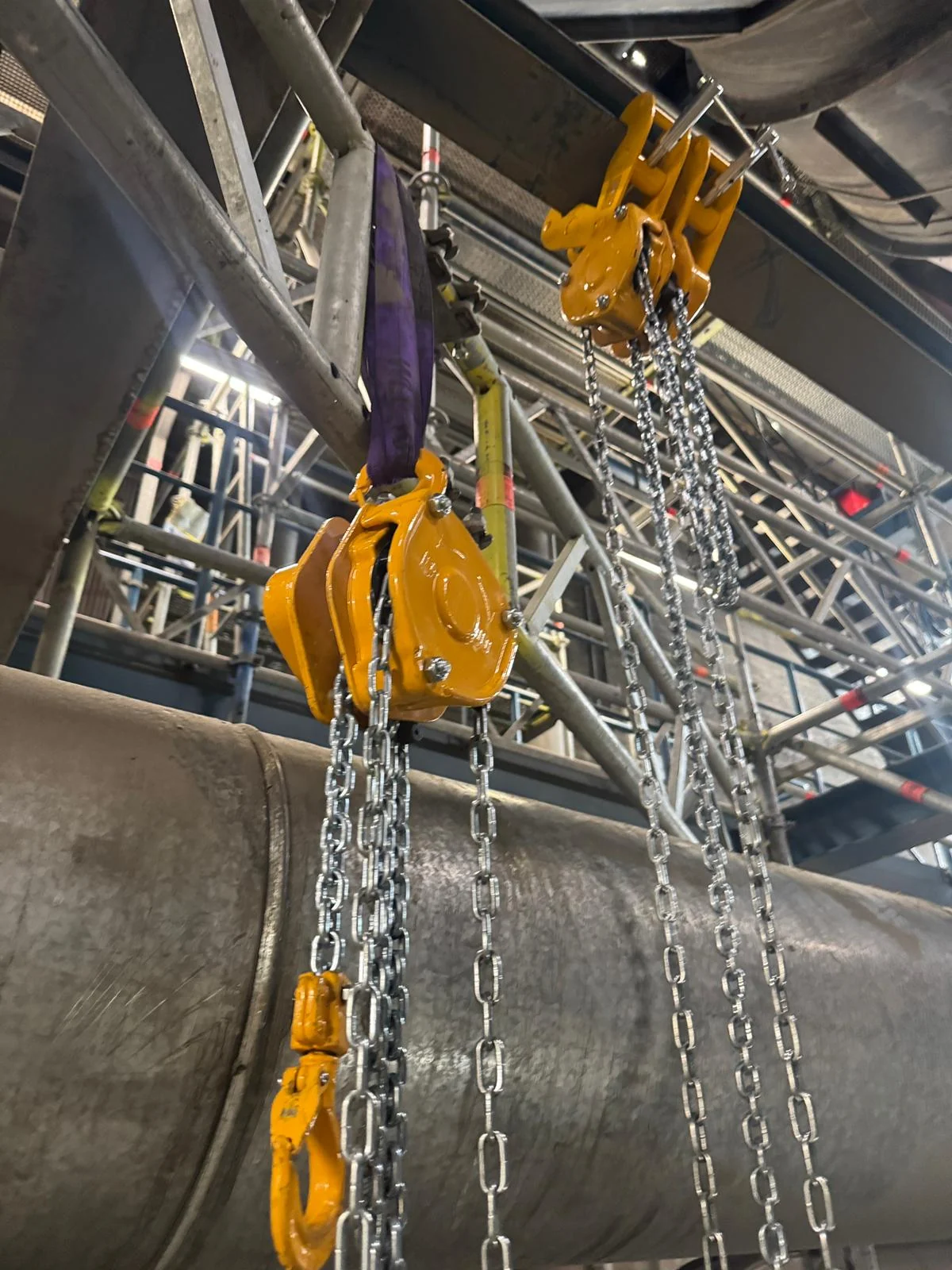 Two beam clamps and chain hoists rigged from overhead steel, taking the weight of a large-bore pipe