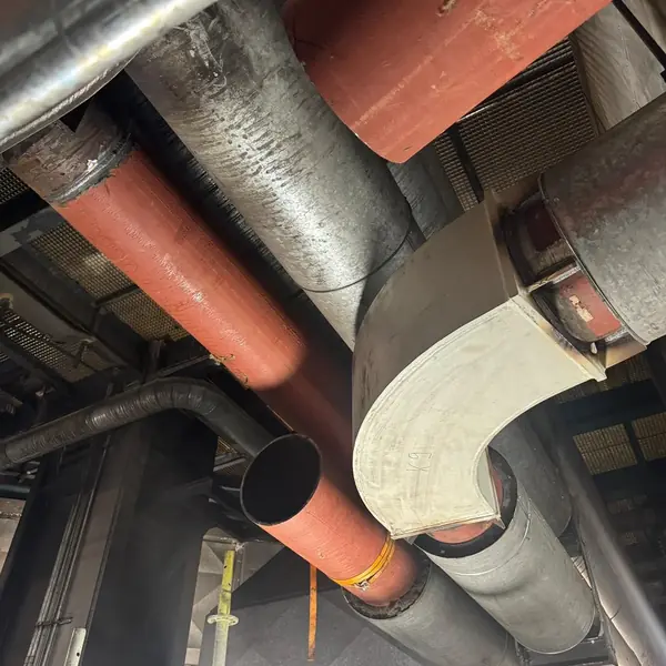 New large-bore pipework and a fabricated bend installed among existing lines and ducts inside an industrial plant