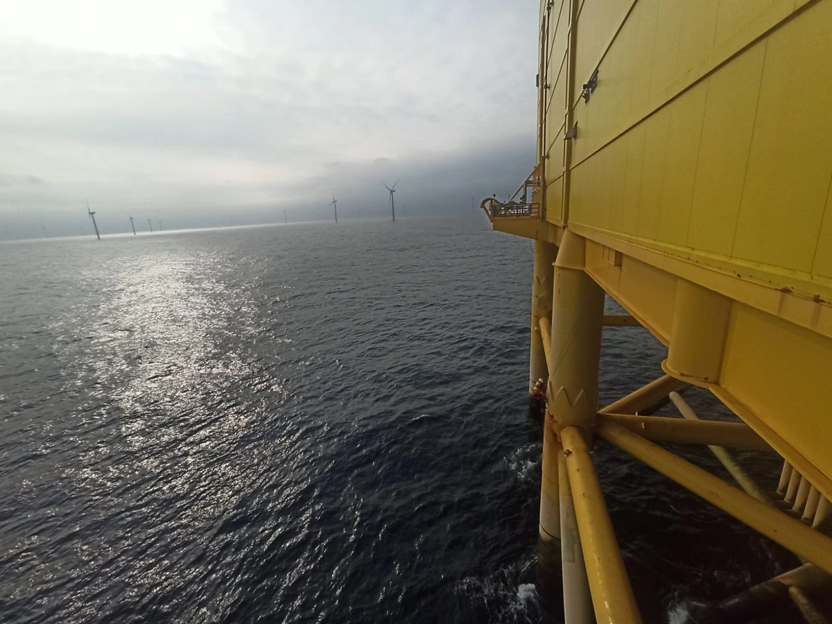 Side of an offshore platform above the sea, with wind turbines in low cloud on the horizon