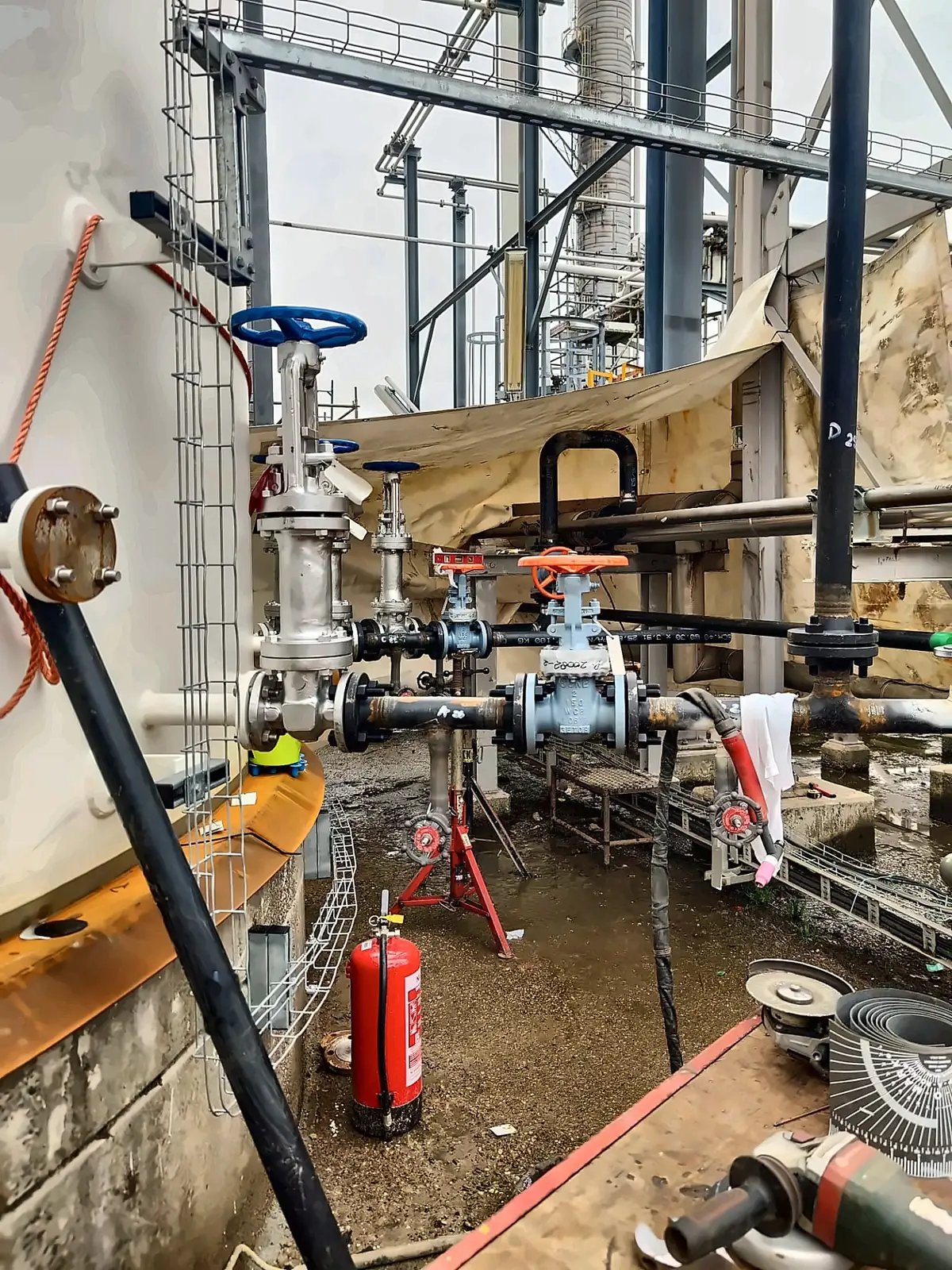Valve station under temporary cover at the base of a storage tank